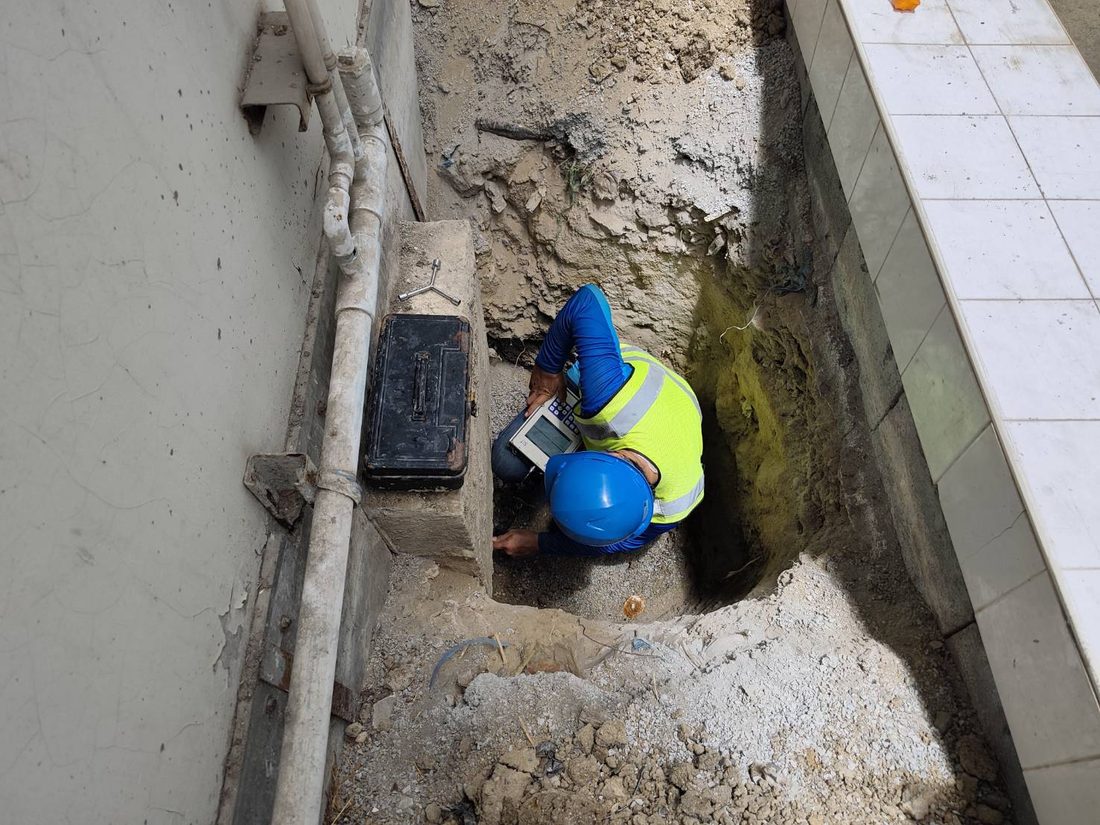 วิศวกรสวมหมวกนิรภัยและเสื้อสะท้อนแสงกำลังทดสอบ Seismic Test ที่ฐานรากอาคารเดิมในหลุมสำรวจข้างผนังอาคาร
