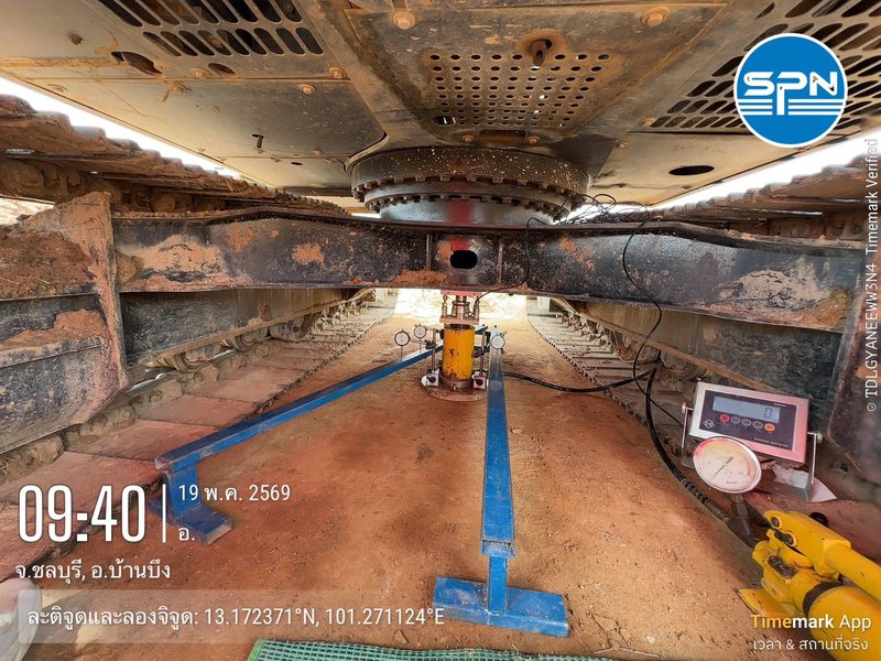 การติดตั้งชุดทดสอบ Plate Bearing Test ใต้ท้องรถแบคโฮที่ใช้เป็นน้ำหนักต้าน พร้อมแม่แรงไฮดรอลิก คานอ้างอิง และเครื่องอ่านค่าแรงกด หน้างานจริงของ SPN