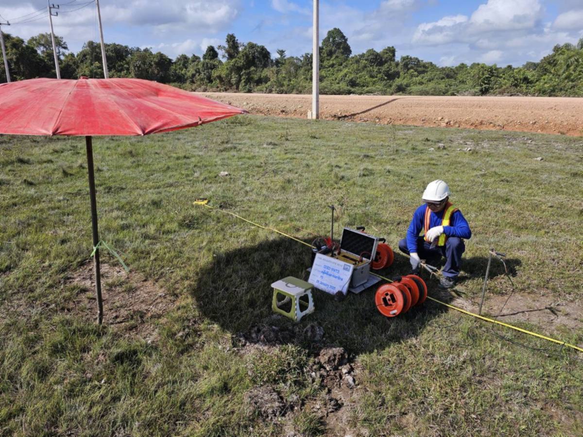 วิศวกรกำลังนั่งย่อตัวต่อสายวัดเข้ากับขา electrode ที่ปักลงดิน มีเทปวัดระยะขึงเป็นแนวตรงเพื่อกำหนดระยะห่างระหว่างขาให้เท่ากัน